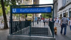Ein Mann und sein Hund gehen eine Straße mit einem Schild mit der Aufschrift „Kurfürstendam“ entlang.