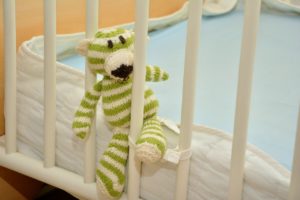 Ein Stofftier schaut verspielt aus einem Kinderbett.