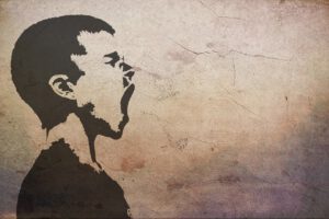 Ein Wandgemälde zeigt das Profil einer Person mit Buzz-Cut-Frisur, die nach links blickt und zu schreien oder zu gähnen scheint. Das Bild ist in schwarzer Farbe auf einer strukturierten, rissigen Wand mit gedämpftem Hintergrund.