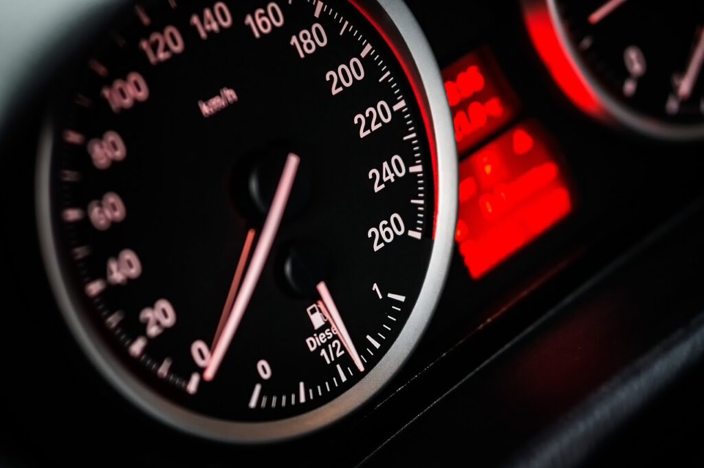 Nahaufnahme eines Autotachometers und einer Tankanzeige. Der Tacho zeigt Geschwindigkeiten von 0 bis 260 Kilometer pro Stunde an, und die Tankanzeige zeigt den Kraftstoffstand an. Das Armaturenbrett ist rot hinterleuchtet.